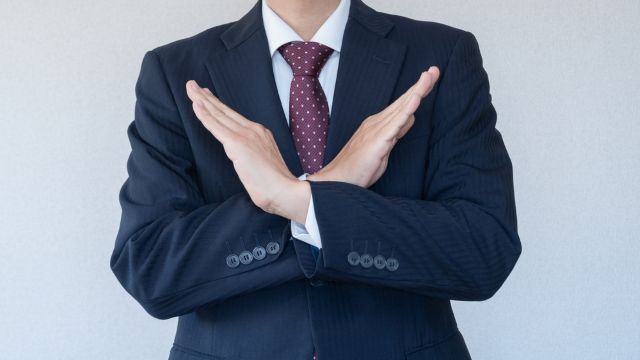 胸の前でバツサインをするスーツの男性